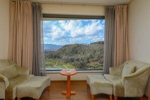 A room with two armchairs and a small table, a large window with curtains, and a view of a hilly landscape. - Huzhiyun Hotel (Chengjiang)