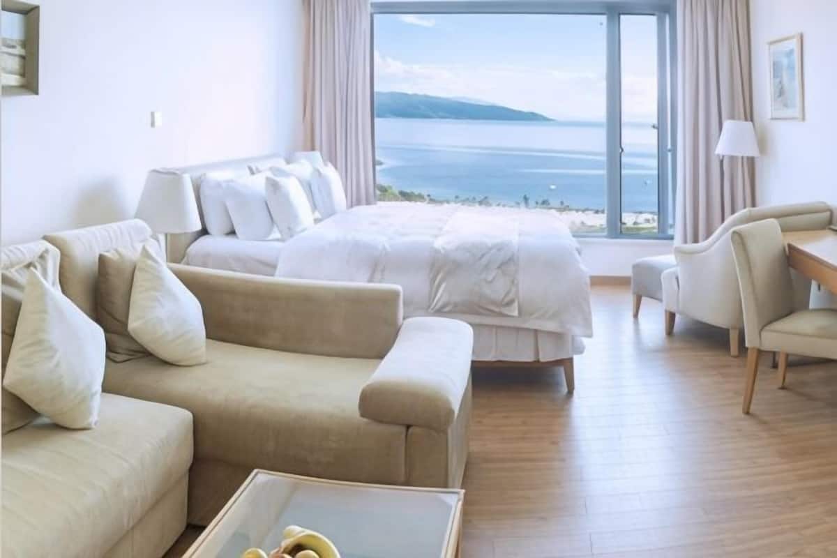 Een hotelkamer met een bed, een bank, een stoel, een bijzettafeltje en uitzicht op zee.