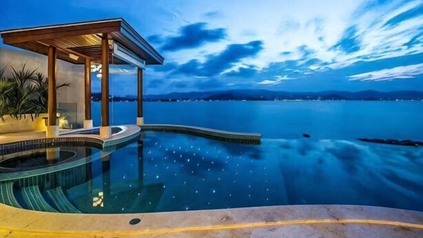 A infinity pool with a wooden deck and a covered seating area overlooking a body of water. - Huzhiyun Hotel (Chengjiang)
