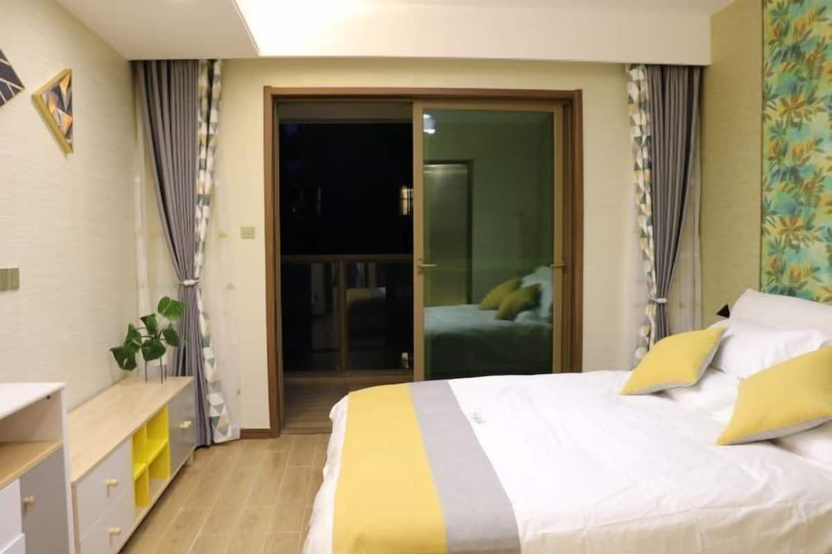 Een slaapkamer met een bed, nachtkastje, een plant en een schuifdeur naar een balkon.