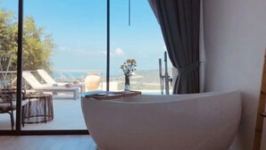 A modern bathroom with a large bathtub, a view of the outdoors, and a table with a vase of flowers. - Huzhiyun Hotel (Chengjiang)