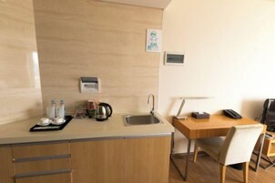 Una kitchenette compacta con un lavamanos, una tetera y una pequeña encimera con botellas y una bandeja.