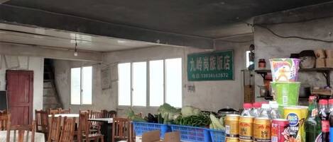 Una habitación con mesas y sillas de madera, un mostrador con alimentos, y un letrero en la pared.