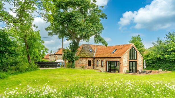 A brick house with a large garden, a patio with outdoor furniture, and a tree in the background. - Waterside Barn, Binham, Norfolk (Binham)