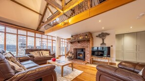 A spacious living room with leather sofas, a fireplace, and a television. - Waterside Barn, Binham, Norfolk (Binham)