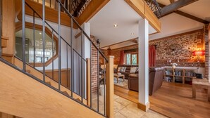 A spacious living area with a wooden staircase, a brick wall, and a cozy seating area. - Waterside Barn, Binham, Norfolk (Binham)