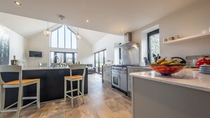 A modern kitchen with a central island, bar seating, and a large window providing natural light. - Waterside Barn, Binham, Norfolk (Binham)