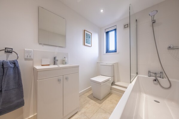 A modern bathroom with a white sink, mirror, toilet, and bathtub.