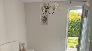 Un dormitorio con cama, mesita de noche, lámpara, candelabro, puerta a un balcón y un cuadro enmarcado en la pared.