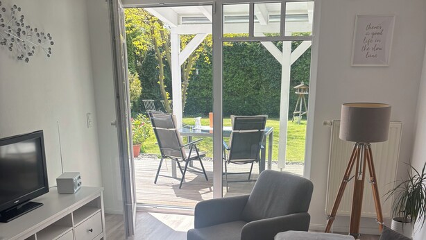 Una sala moderna con un sofá, una mesa de centro con un jarrón, un televisor y un comedor con sillas y una mesa.
