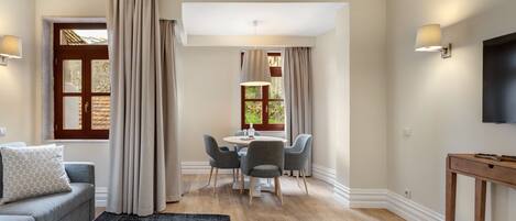 Un salon moderne avec un canapé, une table à manger et des chaises. Il y a un téléviseur accroché au mur et une fenêtre avec des rideaux.