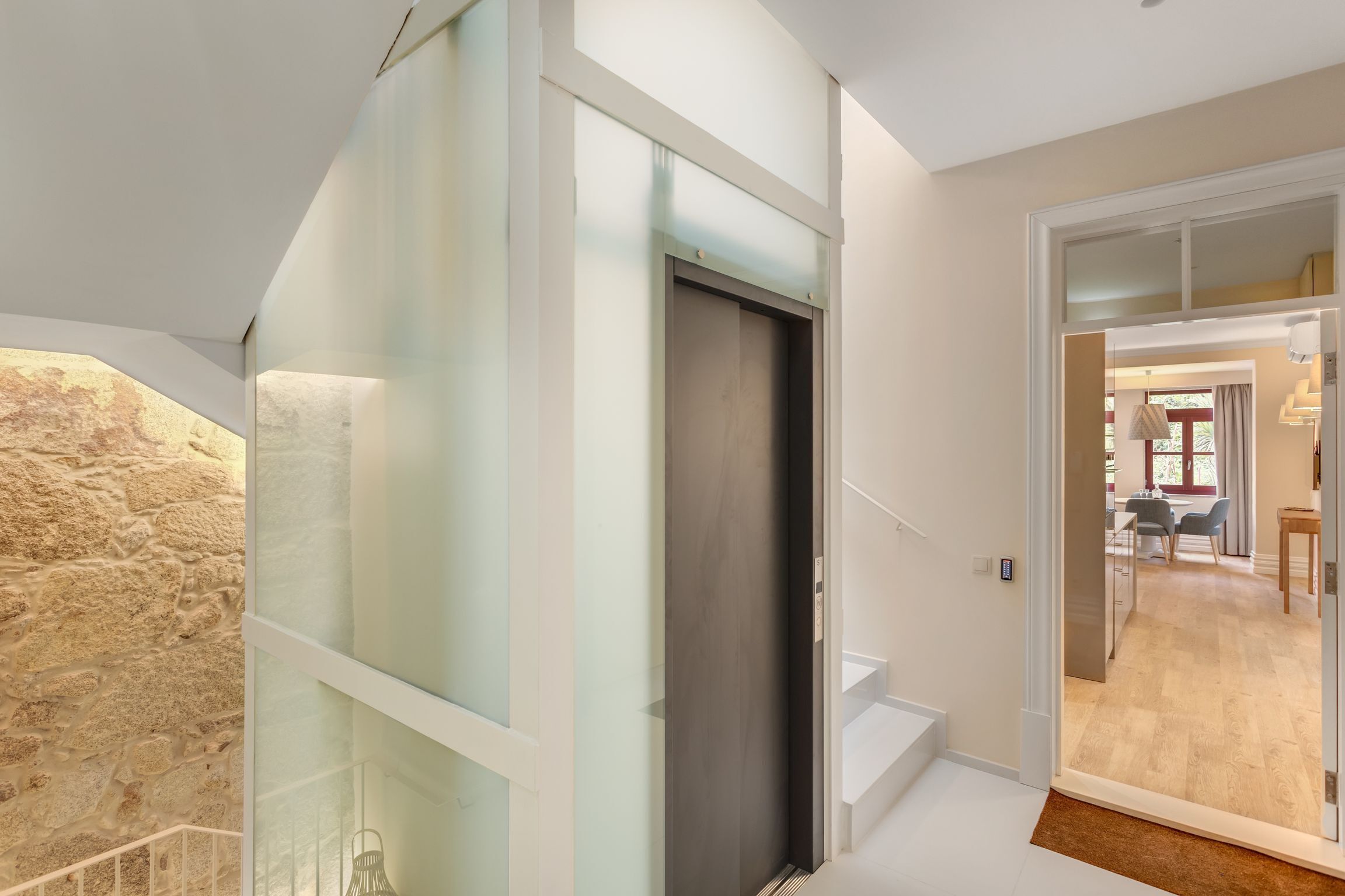 A modern interior with a stone wall, a glass partition, and a dark door leading to a dining area.
