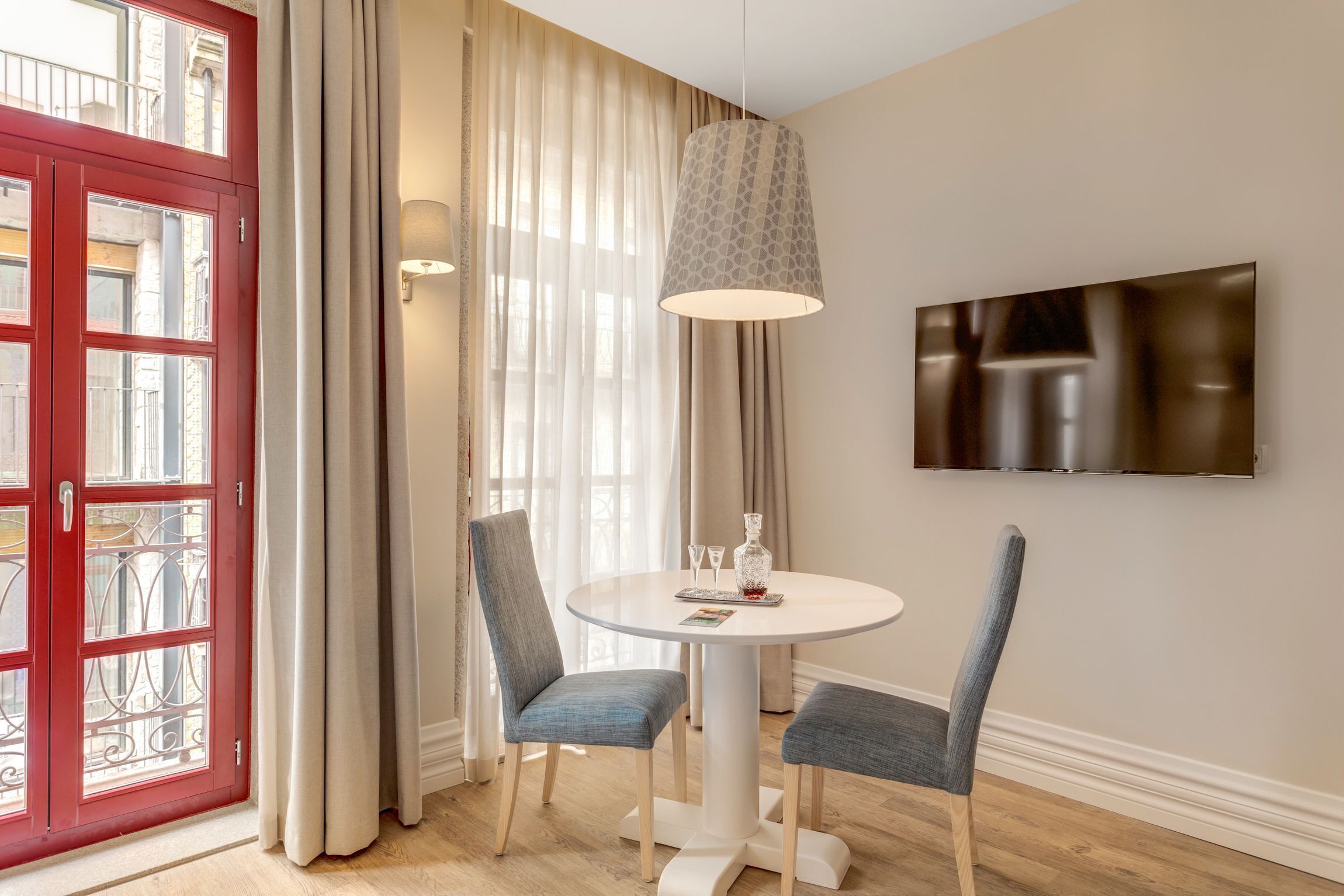 A dining area with a round table, two chairs, a pendant light, and a flat-screen TV on the wall.
