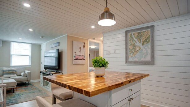 A modern kitchen with a wooden island, white cabinetry, and a hanging pendant light. - New Cottage: 4th row & fully fenced back yard! (Hilton Head Island)