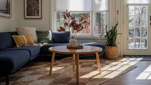 A living room with a blue sofa, a round wooden coffee table, and a potted plant. - Cozy Cottage in Locust Lake w/ Seasonal Lake Views (pocono Lake)