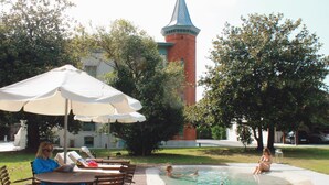 A pool area with a fountain, lounge chairs, and a table with umbrellas.