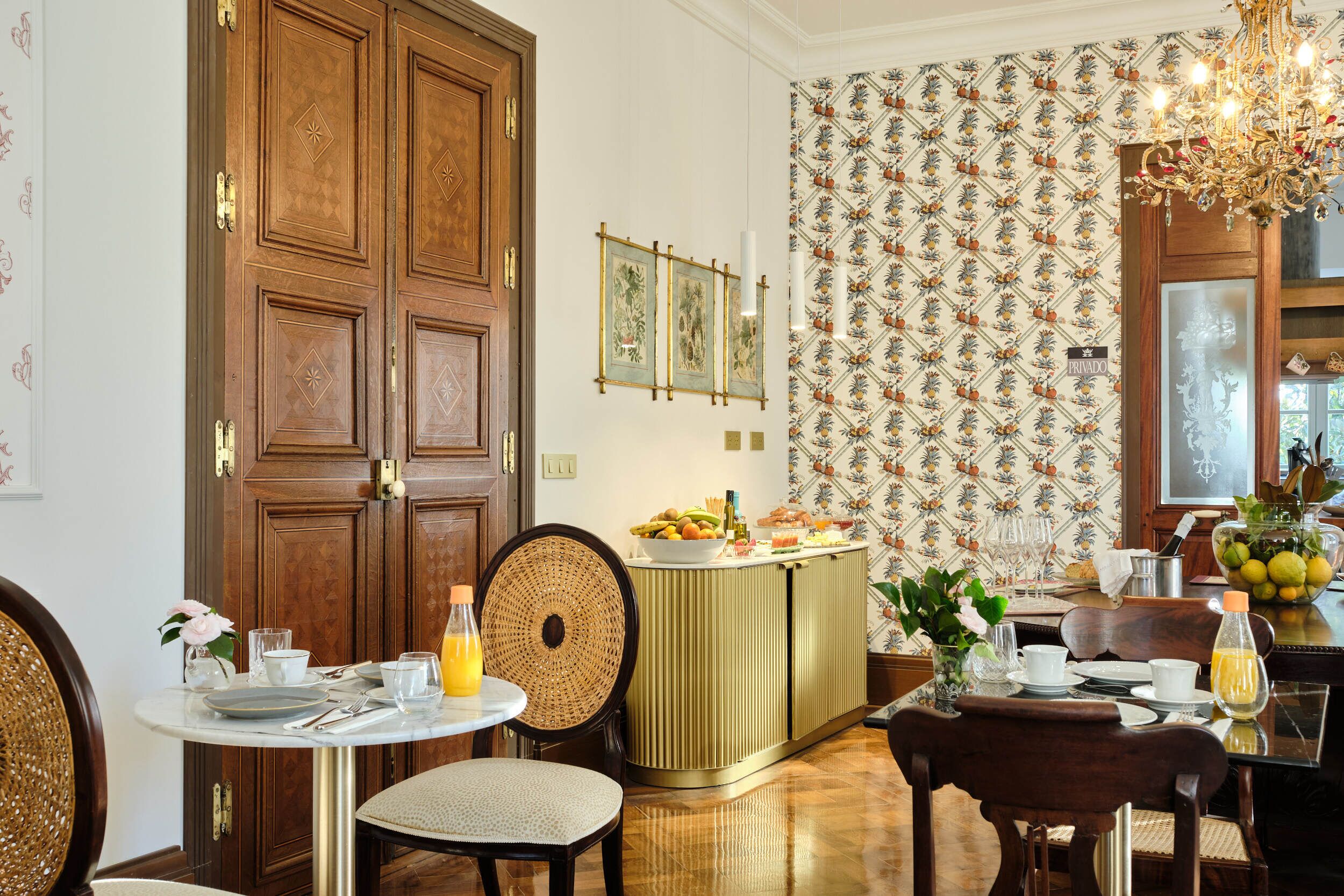 Un comedor con puerta de madera, una mesa de buffet con frutas y bebidas, y un papel tapiz estampado.