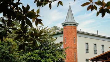 Standing proudly amidst lush surroundings, this historic building boasts a distinctive conical roof atop its traditional brick structure.