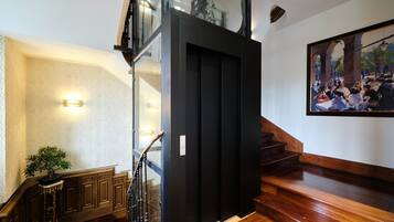 Un escalier avec des marches en bois et une rampe en verre, menant à un ascenseur noir.