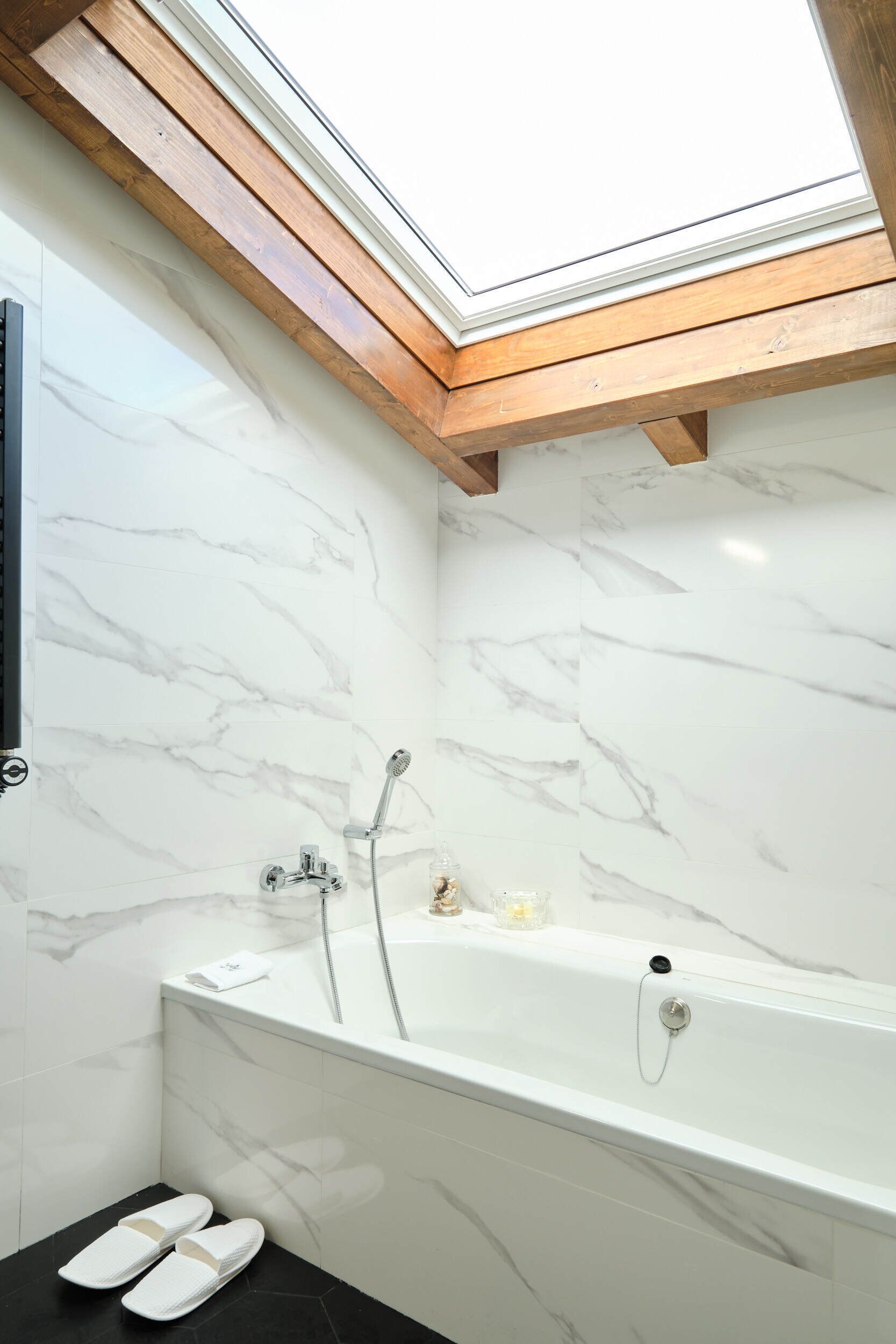 A modern bathroom with a skylight, a bathtub, and marble walls.