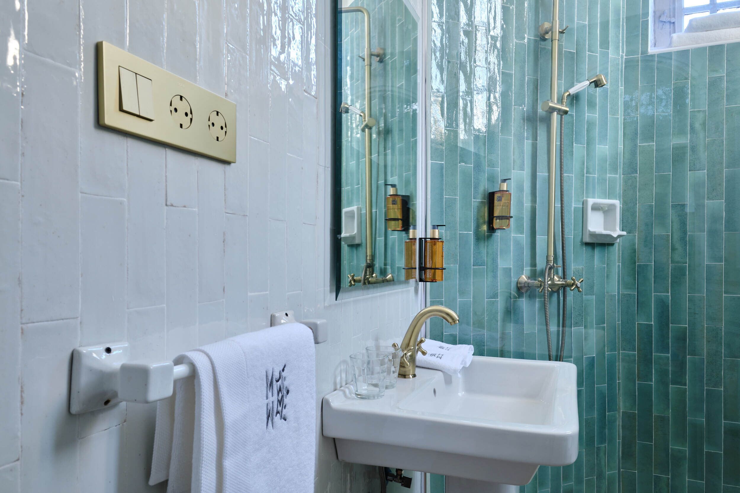 Un bagno con un lavandino bianco, un portasciugamani con un asciugamano bianco, uno specchio e una doccia con rubinetteria dorata.
