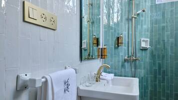 Un bagno con un lavandino bianco, un portasciugamani con un asciugamano bianco, uno specchio e una doccia con rubinetteria dorata.
