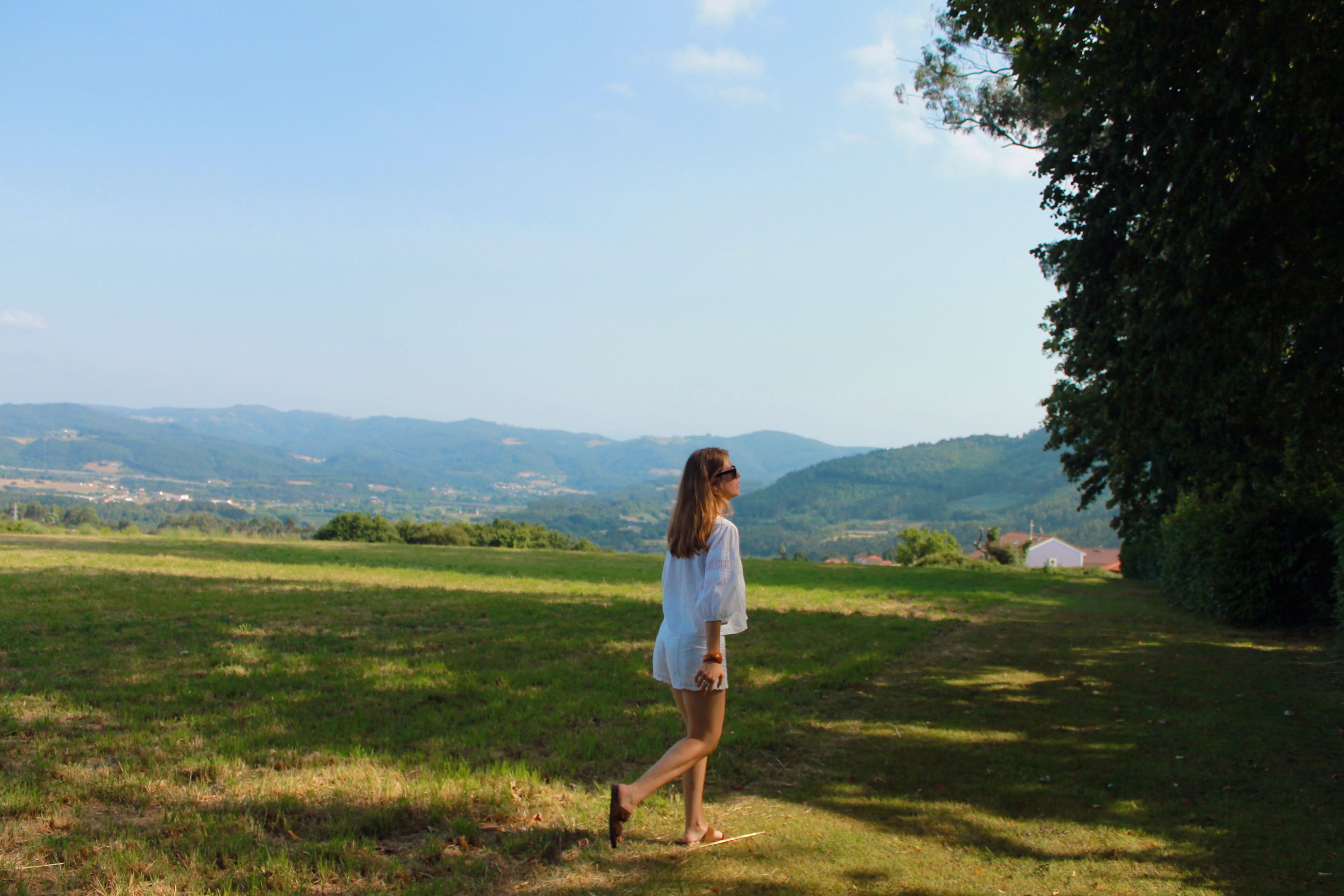 A woman walking on a grassy field with a view of distant mountains and a house in the background.