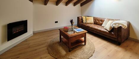 Una habitación estilo loft con vigas de madera a la vista, chimenea, sofá de cuero y tragaluz.