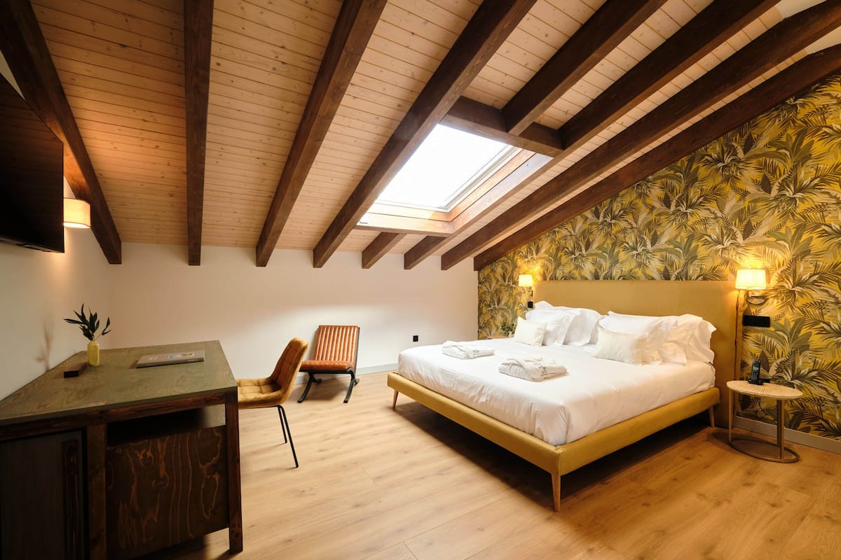 Une chambre avec un plafond en bois, une lucarne, un lit, un bureau, une chaise et une petite table.