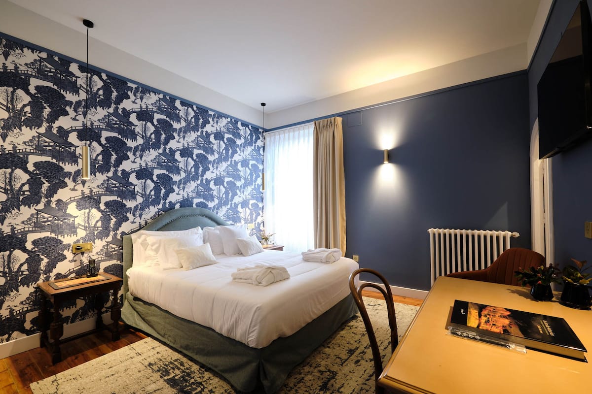 Une chambre à coucher avec un lit, une table de chevet, une lampe et une vue sur l’extérieur.