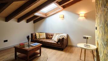 Un dormitorio estilo loft acogedor con techo inclinado, un sofá de cuero, una mesita redonda y una lámpara de pared.