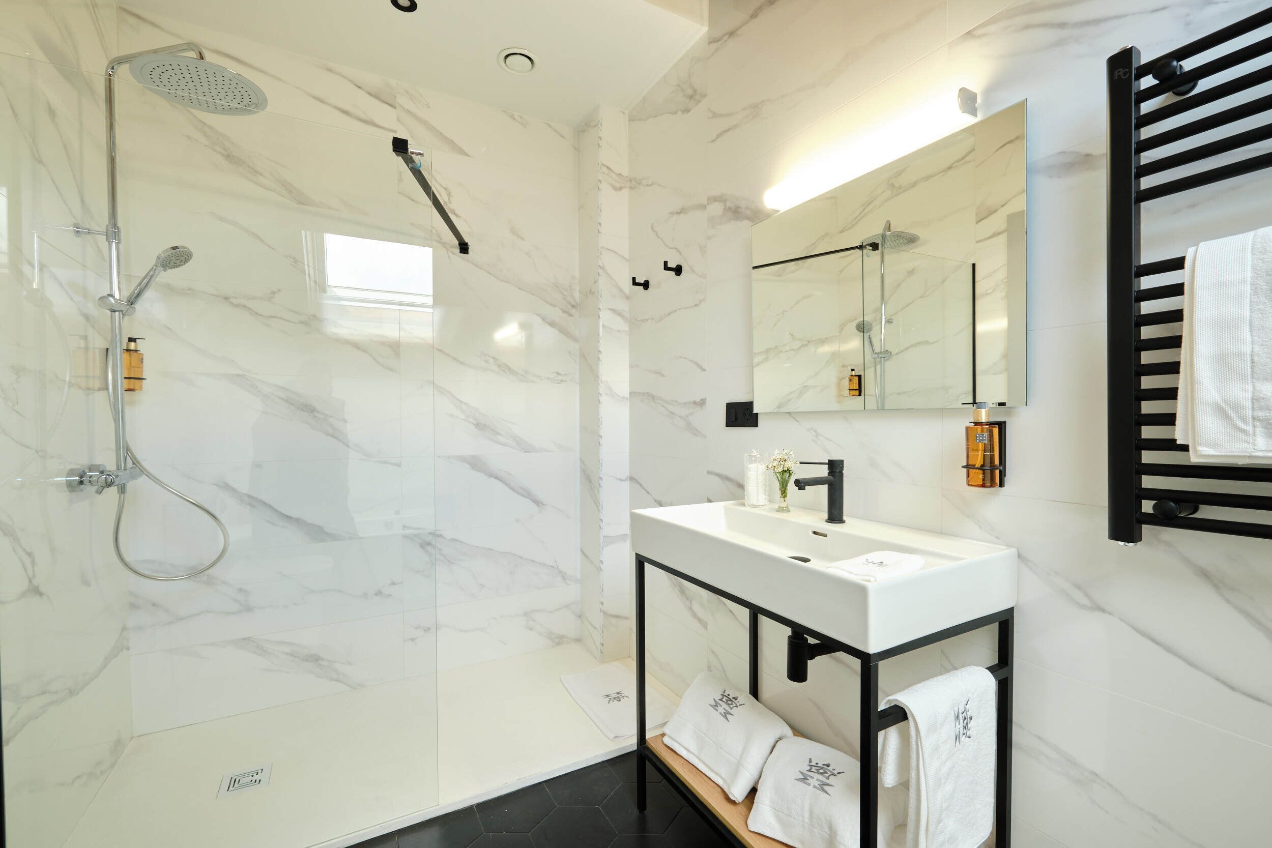 Une salle de bain moderne avec une douche à parois de verre, un lavabo en marbre blanc et un porte-serviettes noir.