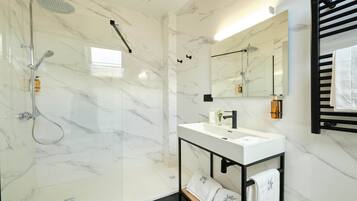 Une salle de bain moderne avec une douche à parois de verre, un lavabo en marbre blanc et un porte-serviettes noir.