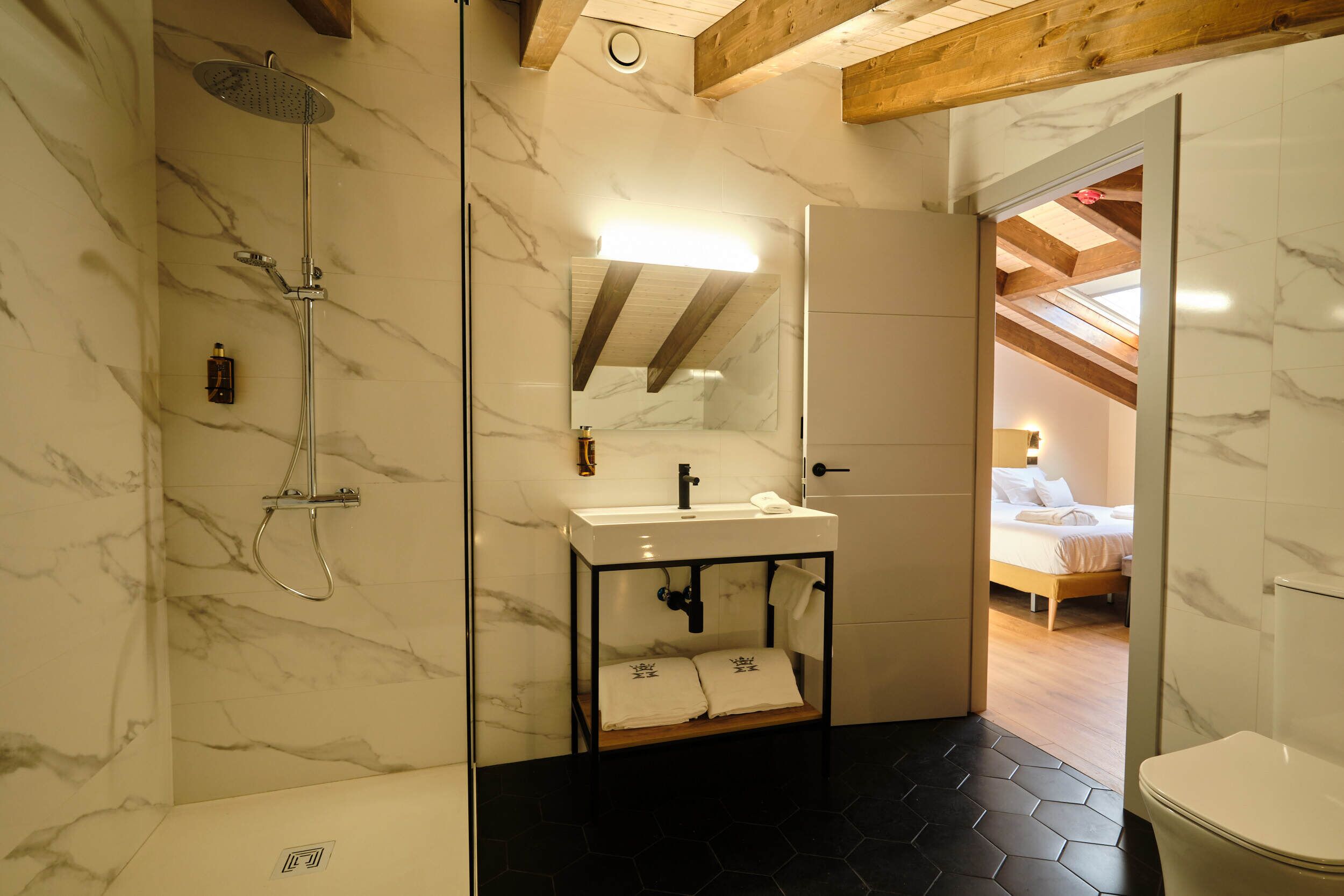 A bathroom with a shower, sink, and toilet, marble walls, and a wooden ceiling.