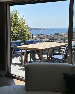 A balcony with a wooden table and blue chairs, overlooking a coastal cityscape. - Mona Bosphorus  (Istanbul)