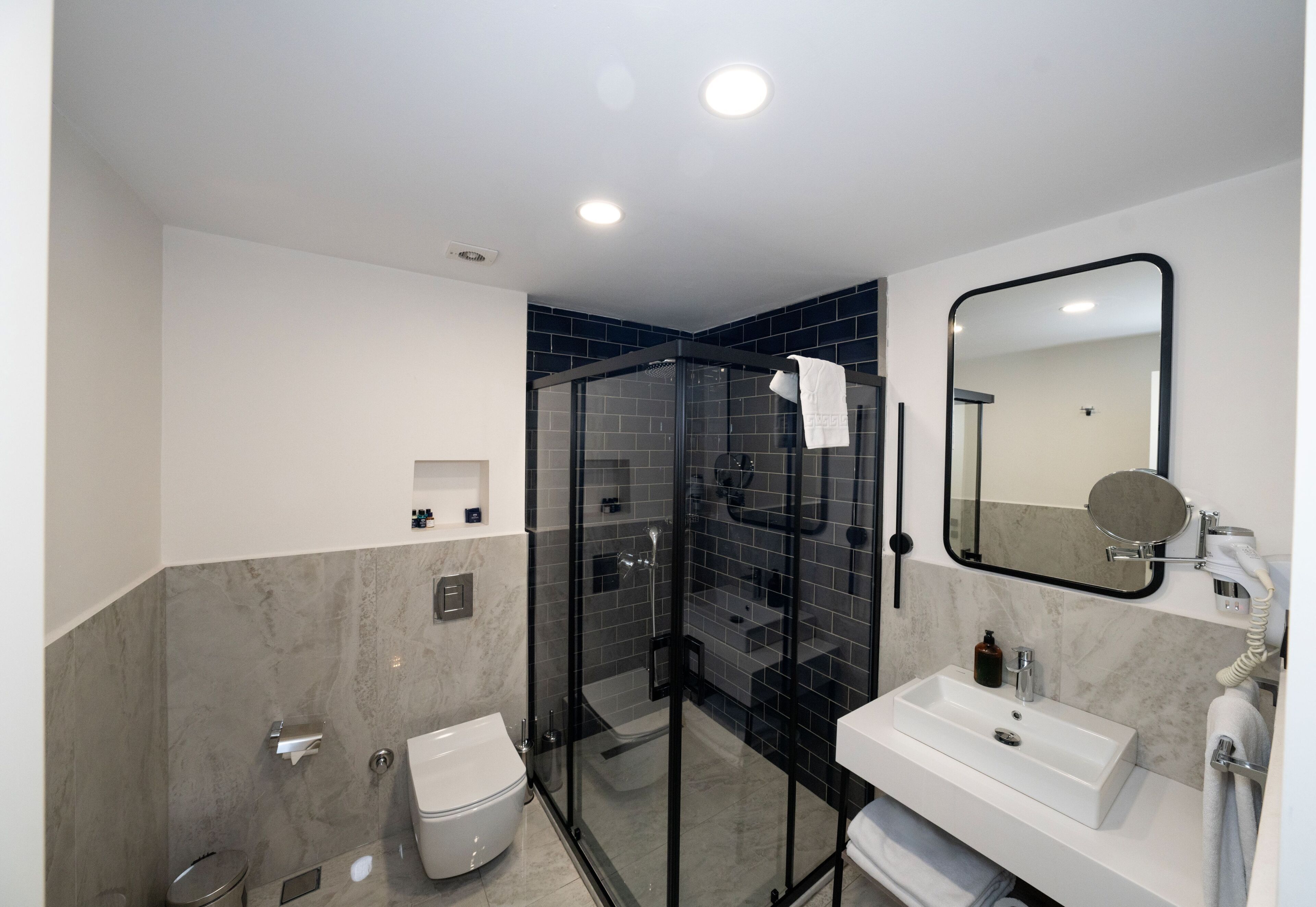 A modern bathroom with a glass-enclosed shower, a white sink, and a large mirror.