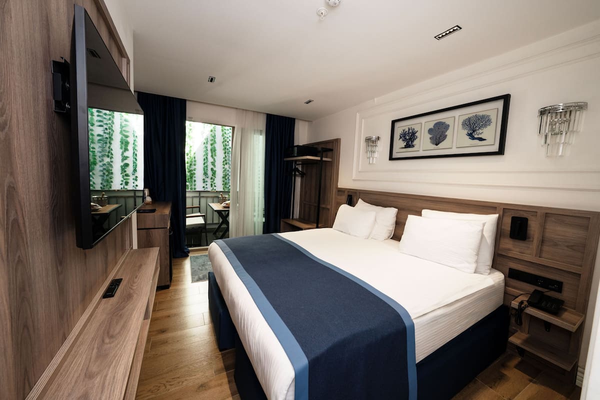Een hotelkamer met een groot bed, een aan de muur bevestigde televisie, een bureau met stoel en een raam met gordijnen.