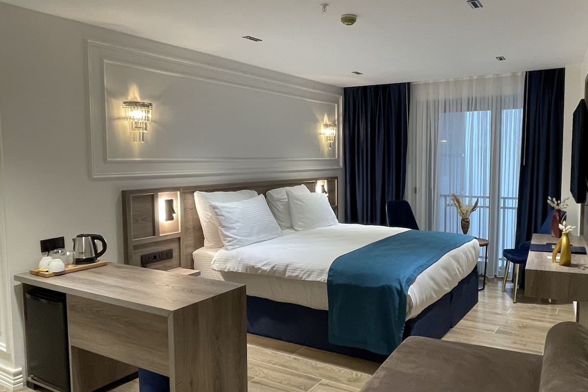 Een hotelkamer met een bed, nachtkastje, lamp en uitzicht op de omgeving.