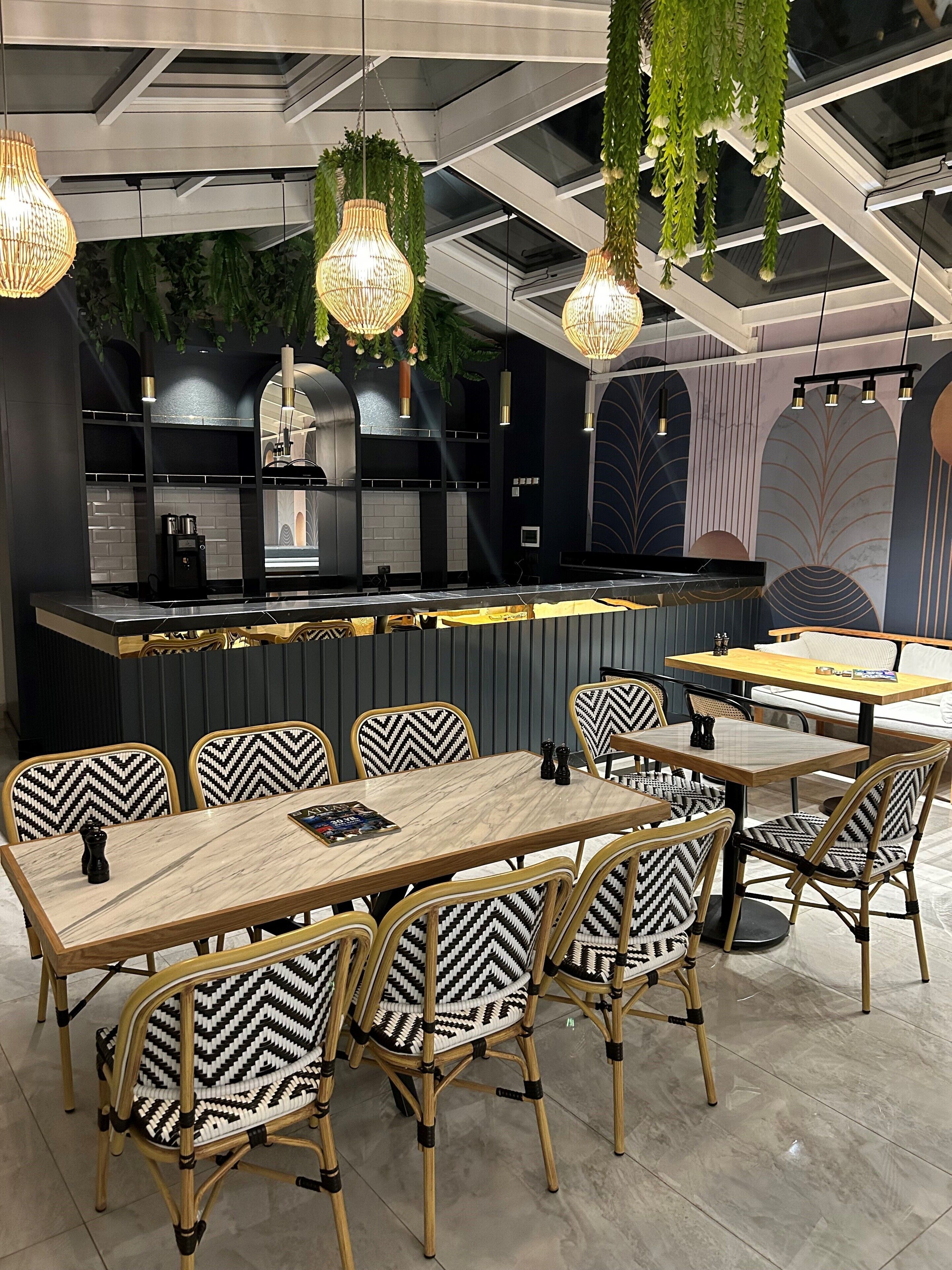 A modern restaurant interior with a central bar, black and white patterned chairs, hanging light fixtures, and a ceiling with skylights.