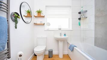 A modern bathroom with a toilet, sink, and bathtub. There are shelves with plants and toiletries.