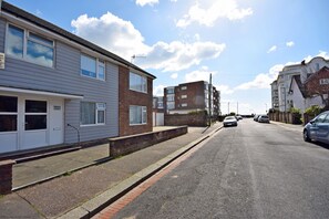 A residential street with houses, a clear sky, and parked cars.