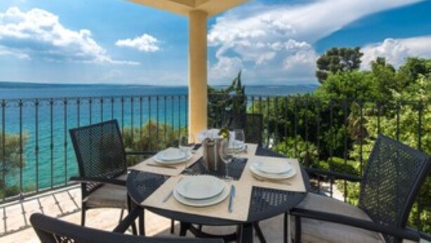 A dining table set on a balcony with a view of the sea and greenery. - 4-star apartments with direct beach access in front of the house (Crikvenica)