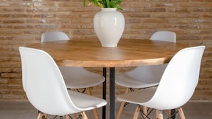 Une table ronde en bois, entourée de quatre chaises blanches, un vase blanc rempli de fleurs et un mur en briques en arrière-plan.