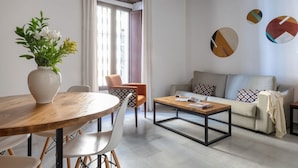 Un salon moderne avec une table ronde en bois, des chaises blanches, un canapé gris agrémenté de coussins à motifs et une table basse.