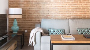 Una sala de estar con pared de ladrillo, un sofá, una mesa de centro, una l ámpara y un televisor.