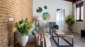 A living room with a brick wall, a sofa, a green armchair, a coffee table, and a potted plant.