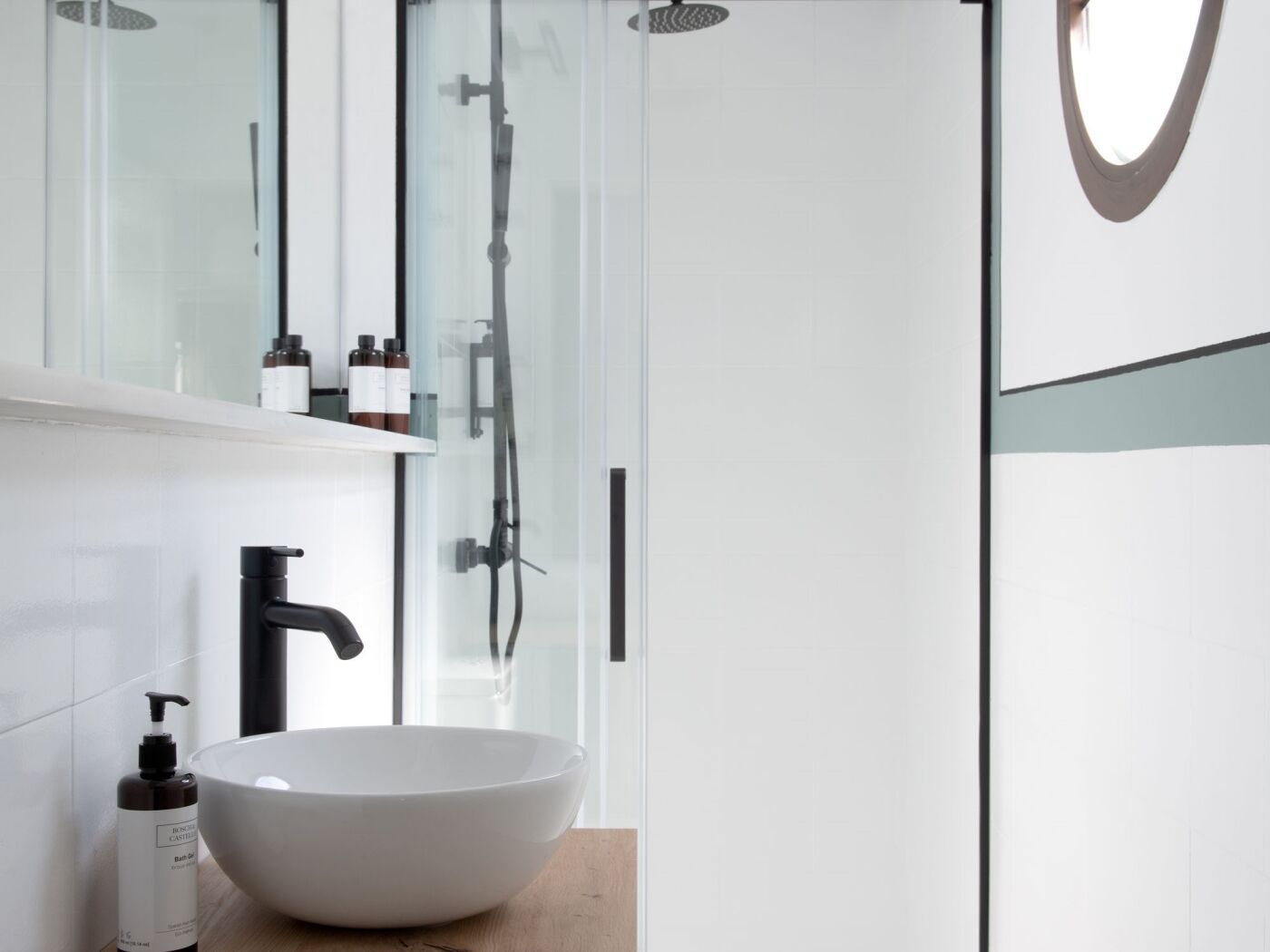 Un bagno moderno con un lavandino bianco ampio, un rubinetto nero e un box doccia in vetro.