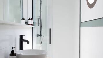 Un bagno moderno con un lavandino bianco ampio, un rubinetto nero e un box doccia in vetro.