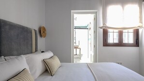 A bedroom with a large bed, a headboard, a window with curtains, and a view of the outside.