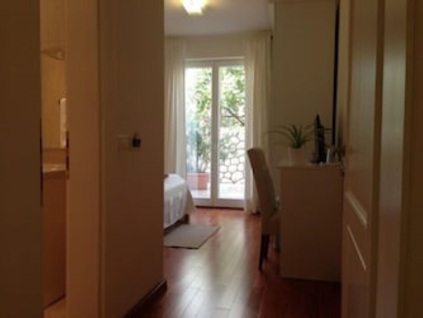 A narrow hallway leading to a room with a bed, a chair, and a small table.
